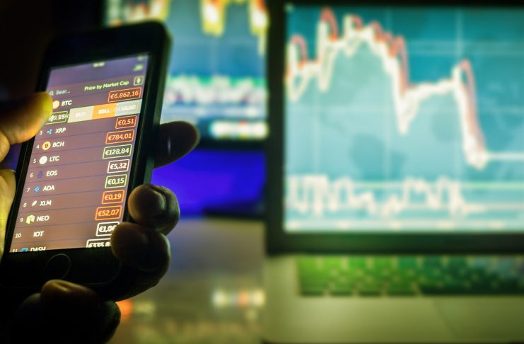 Day trader using mobile phone and computer screens with charts, Vienna Austria, 25-3-2018